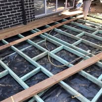 Timber deck frame with joists and bearers under construction against a brick wall
