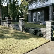 Brick-and-block low front fence with brick pillars in front of a two-storey brick house