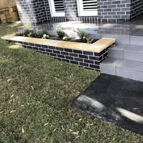 Brick garden bed with new plantings next to tiled front steps
